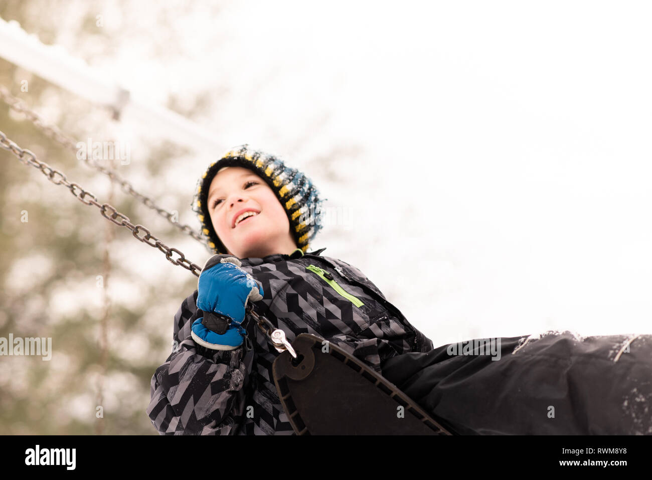 Junge in Strick Hut schwingen auf Spielplatz Schaukel im Winter Stockfoto