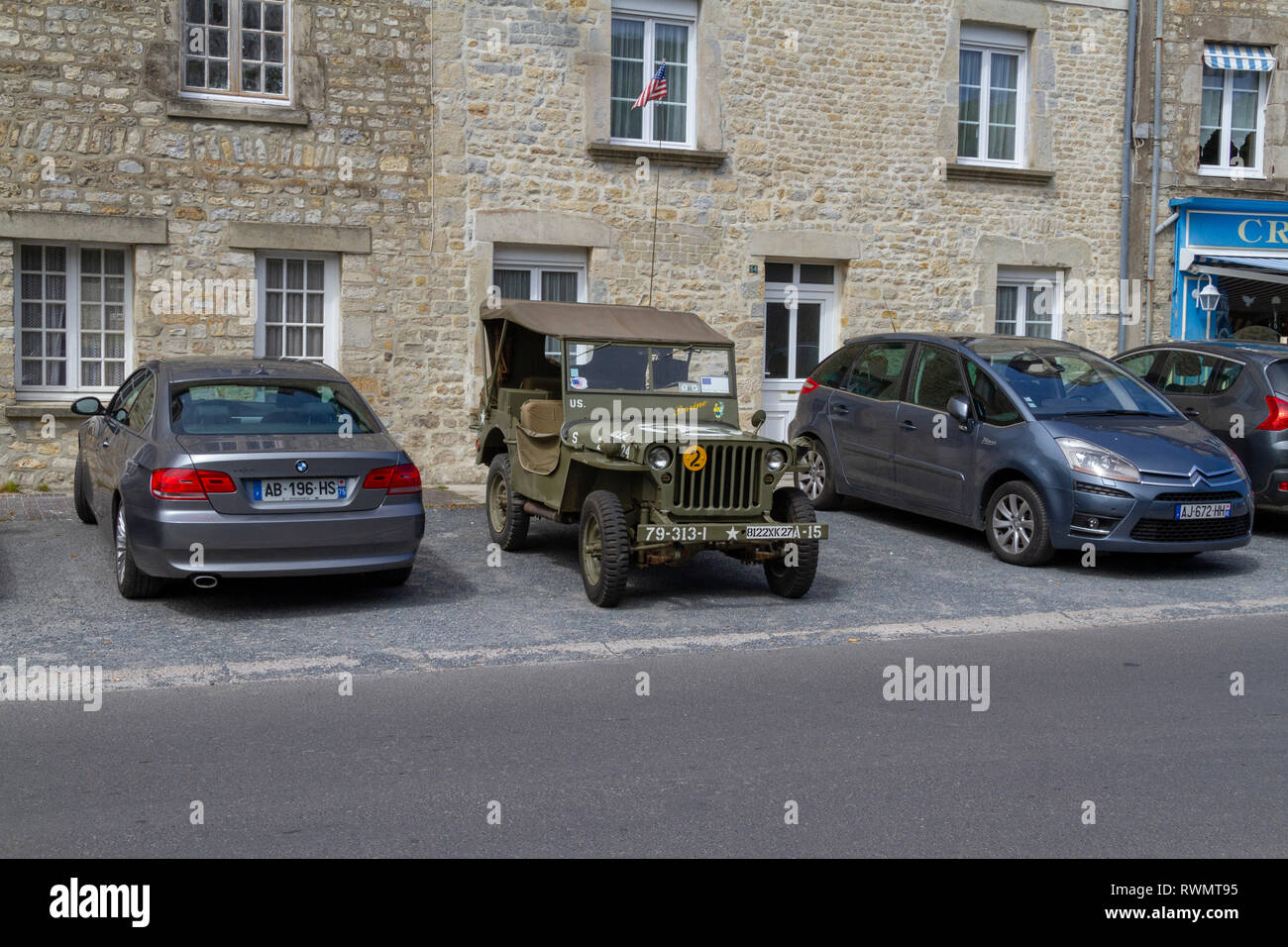 Die US-Armee Weltkrieg zwei Jeep zwischen zwei moderne Autos in Sainte-Marie-du-Mont, Normandie, Frankreich geparkt. Stockfoto