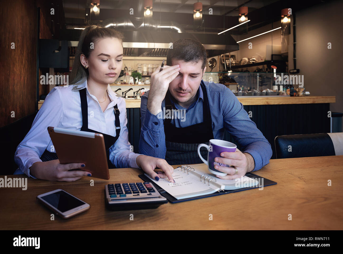 Junge Unternehmer über Dokumente im Restaurant. Auf tisch Telefon, Tablet, Tasse Kaffee, Notebook Stockfoto