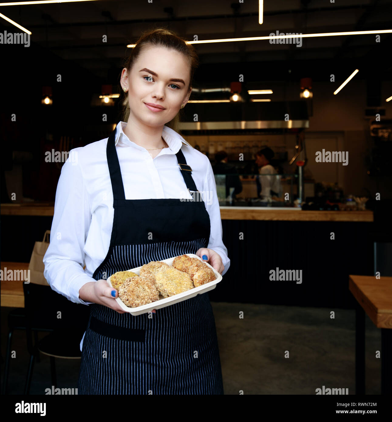 Lächelnde junge Frau mit frischer Petersilie. Blurry restaurant Zähler und Mitarbeiter im Hintergrund arbeiten Stockfoto