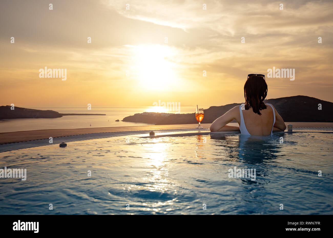 Frau im Infinity-pool an den goldenen Sonnenuntergang. Mädchen bewundern Sie den Sonnenuntergang vom Pool mit einem Cocktail in der Nähe. Sommer Urlaub Stockfoto