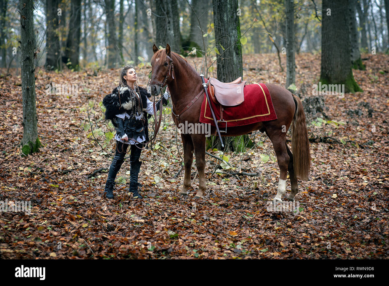 Krieger Schönheit mit ihrem Pferd in den Wald. Viking Frau. Rekonstruktion eines mittelalterlichen Krieg Szene im Wald, im Herbst. Stockfoto