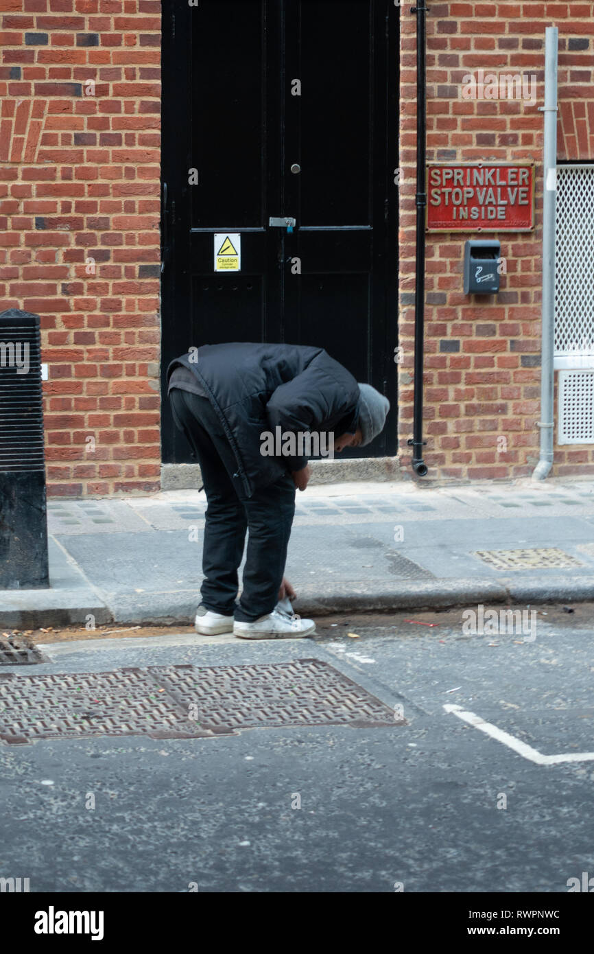 Obdachlose, die London Street ältere Menschen bücken suchen die Straße Rinne für verwendet und entsorgte Zigarettenkippen Stockfoto