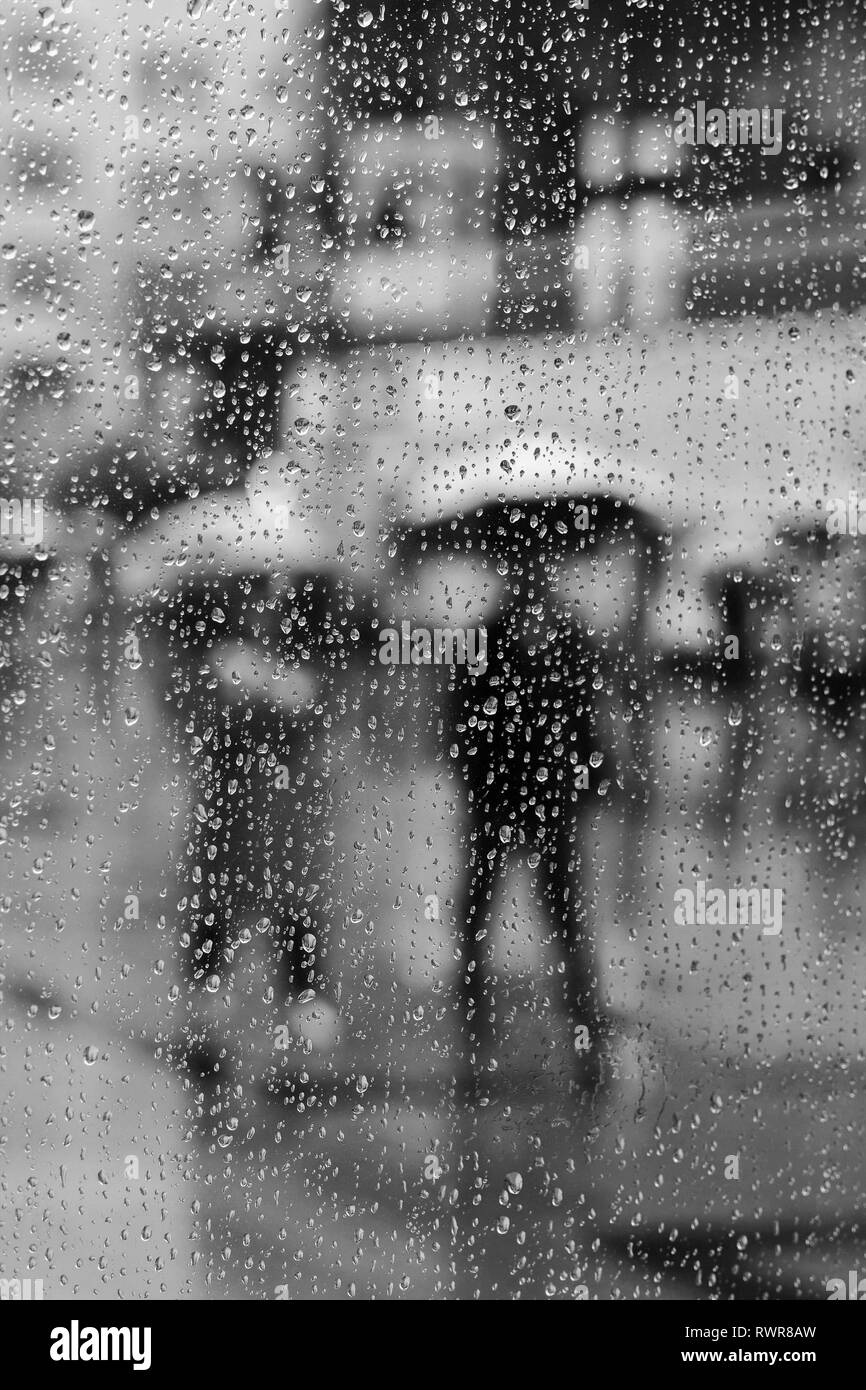 Durch ein Fenster in der Regen fällt und die Menschen gehen vorbei mit Sonnenschirmen. Stockfoto
