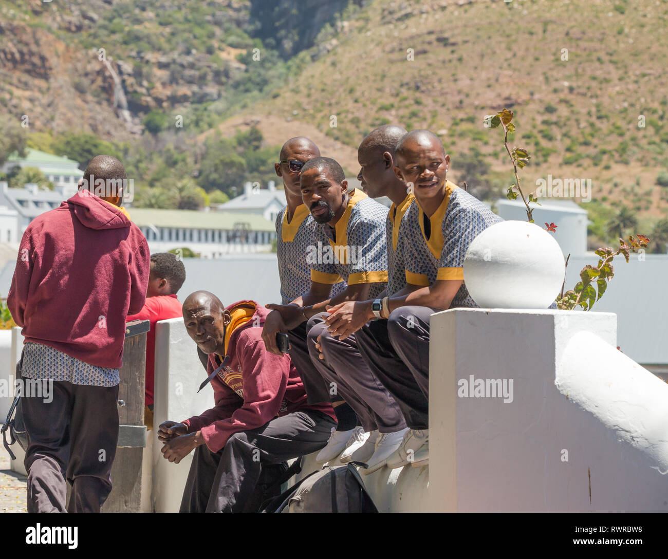 Gruppe der afrikanischen Männer in traditionellen afrikanischen Design und Muster shirts sitzen auf einer Mauer im Freien in Simonstown, Kap, Südafrika gekleidet Stockfoto