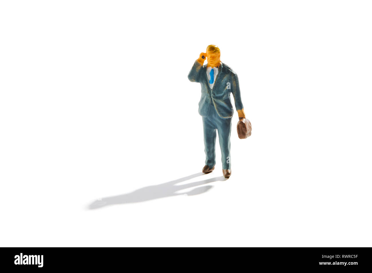 Miniatur Geschäftsmann mit Aktenkoffer über ein Mobiltelefon ein Gespräch wie geht er mit Schatten auf weißem Stockfoto