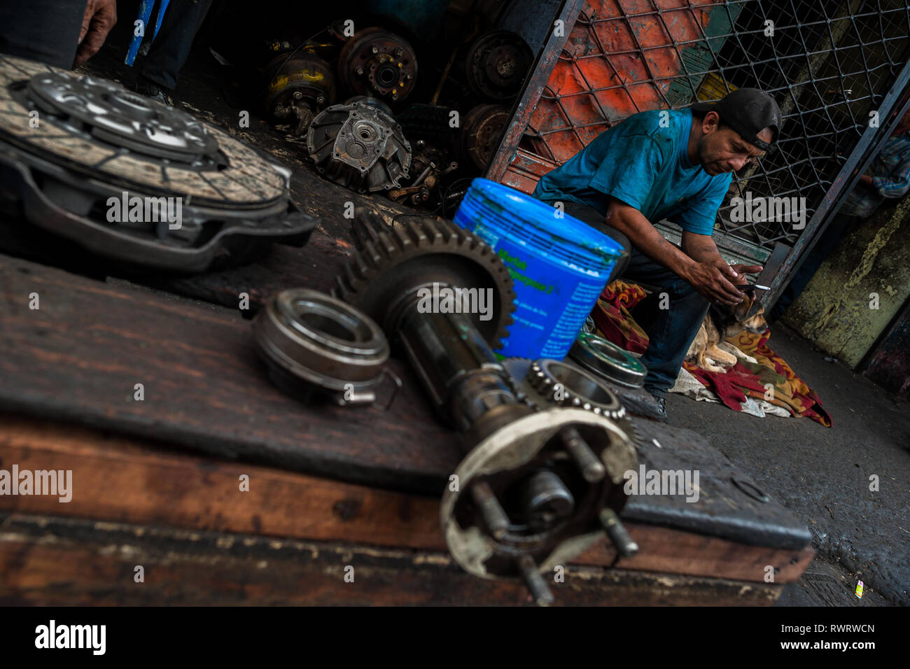 Eine kolumbianische Automechaniker liest ein Mobiltelefon vor eine Autowerkstatt im Barrio Triste, Medellín, Kolumbien. Stockfoto