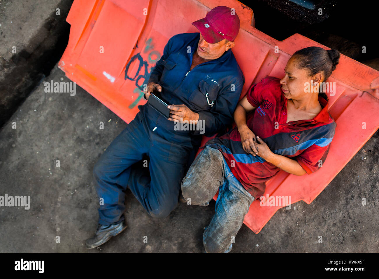 Kolumbianische Automechaniker lesen Ein Handy Bildschirm während einer Arbeitspause auf der Straße im Barrio Triste, Medellín, Kolumbien. Stockfoto