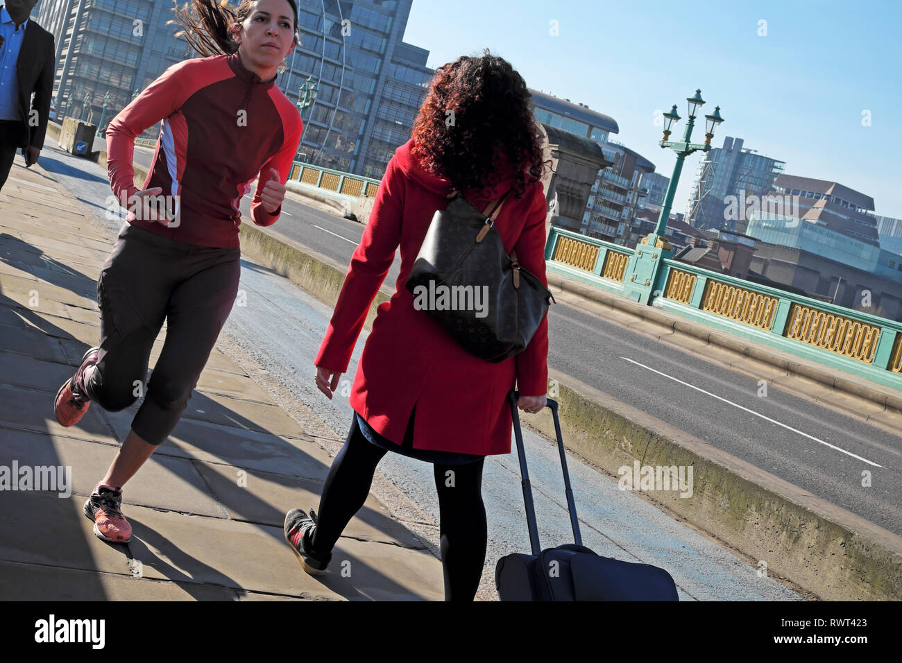 Eine junge Frau, die in Lycra über die Southwark Bridge und eine Person mit Gepäck zu Fuß an einem sonnigen Tag im Winter London England UK KATHY DEWITT Stockfoto