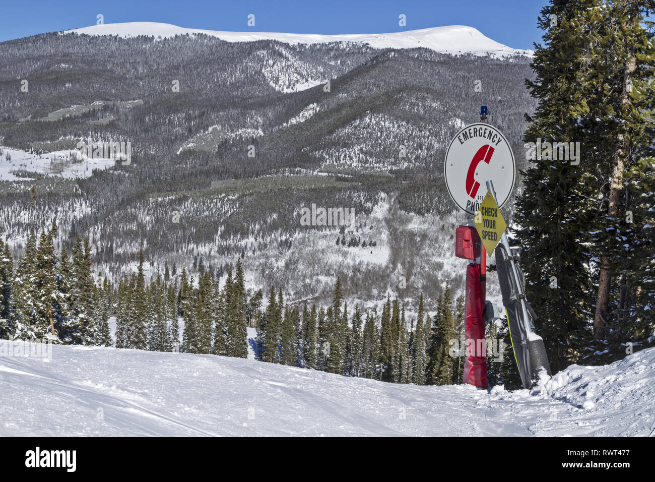Notrufzeichen und Geschwindigkeitskontrollschild auf einem schneebedeckten Berghang in einem Skiresort in Colorado, USA, mit den Rocky Mountains im Hintergrund Stockfoto