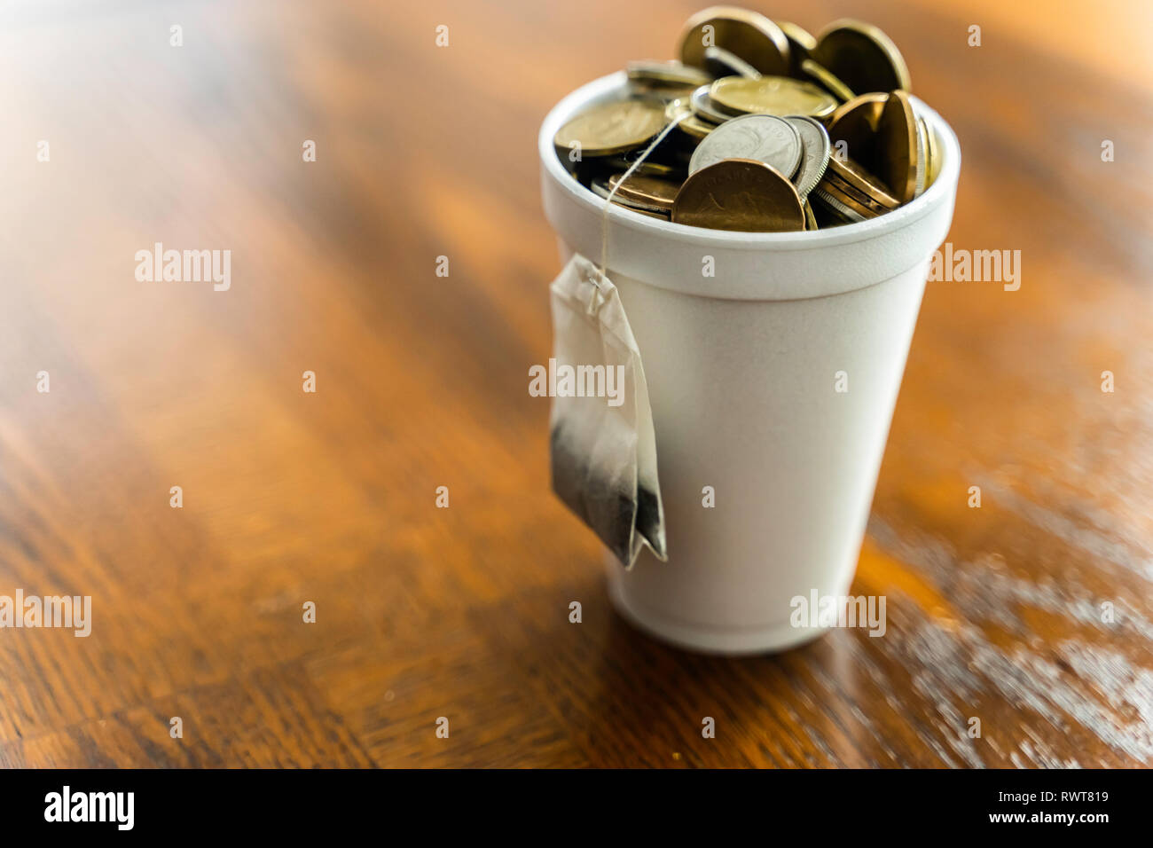 Styroporbecher gefüllt mit Münzen und Teebeutel außerhalb hängend Stockfoto