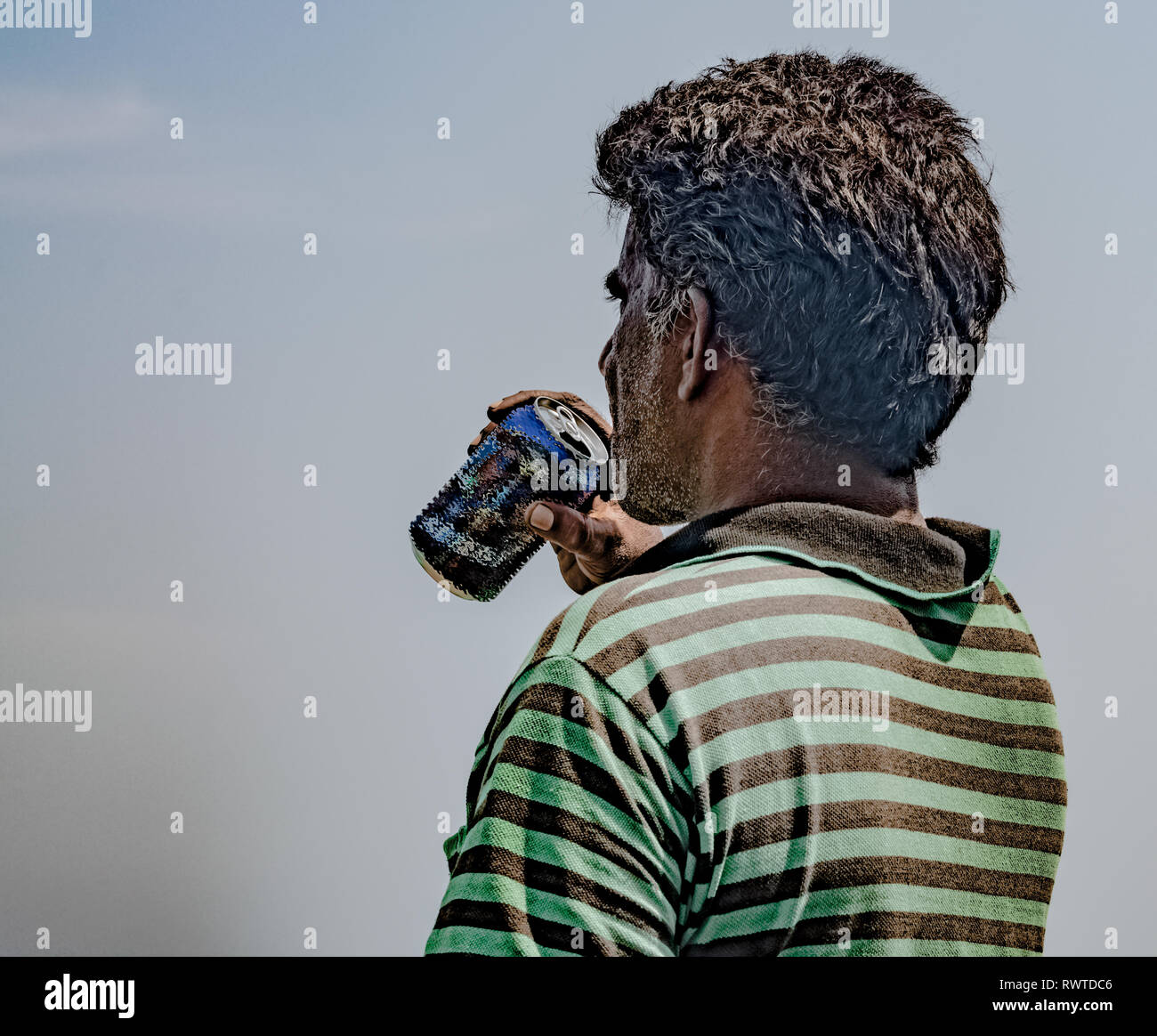 Im mittleren Alter Fischer der asiatischen Ursprungs, das Tragen von gestreiften T-Shirt ist erschöpft und Abschrecken, seinen Durst durch das Trinken von Bier/kaltes Getränk an einem heißen sonnigen Tag Stockfoto