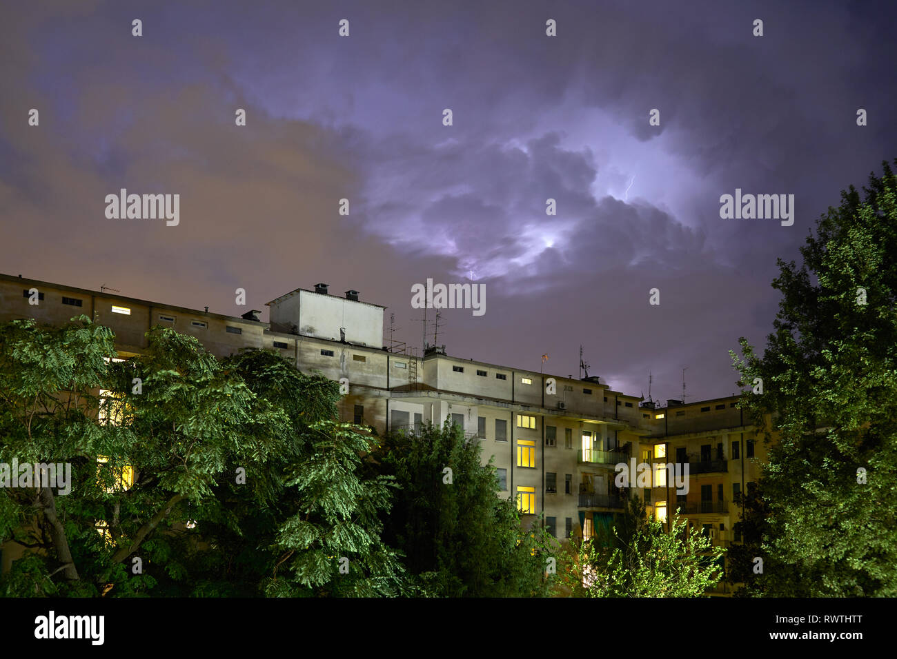 Gebäude und grüne Bäume bei Nacht, beleuchtete Himmel während eines Gewitters in Italien Stockfoto