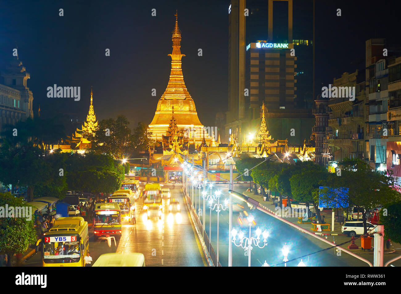 YANGON, MYANMAR - 15 Februar 2018: Am Abend Blick auf Sule Straße mit zahlreichen öffentlichen Busse und die riesigen goldenen hell beleuchteten Stupa von Sule P Stockfoto