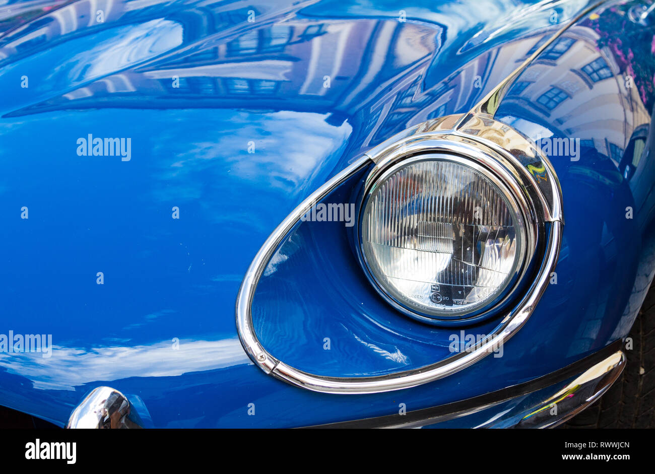 Nahaufnahme der Scheinwerfer der Jaguar E-Type-Serie 2 mit Spiegelungen alter Gebäude auf der Oldtimer-Ausstellung in Sopron, Ungarn Stockfoto