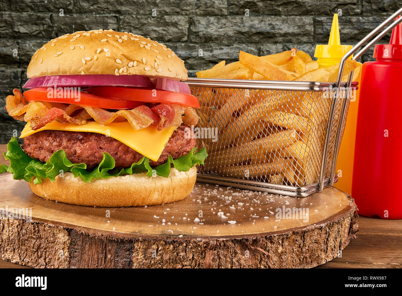Cheeseburger mit Rindfleisch Patty und Speck. Pommes frites in Korb, Ketchup und Senf Flasche im Hintergrund. Auf Mauer getrennt. Real close up. Stockfoto