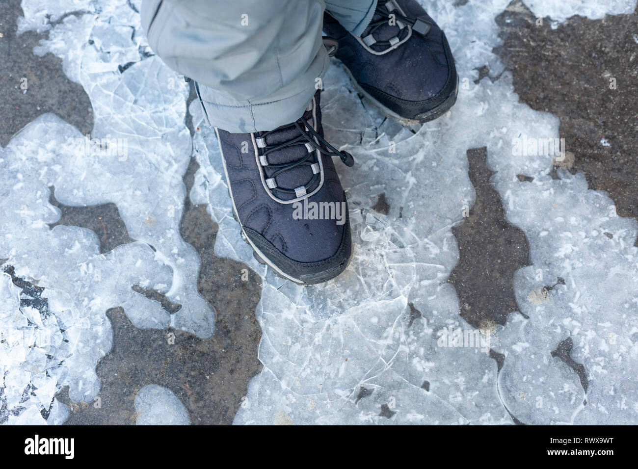 Kind Schritte auf gefrorenen Pfütze mit dünnem Eis. Close Up. Stockfoto