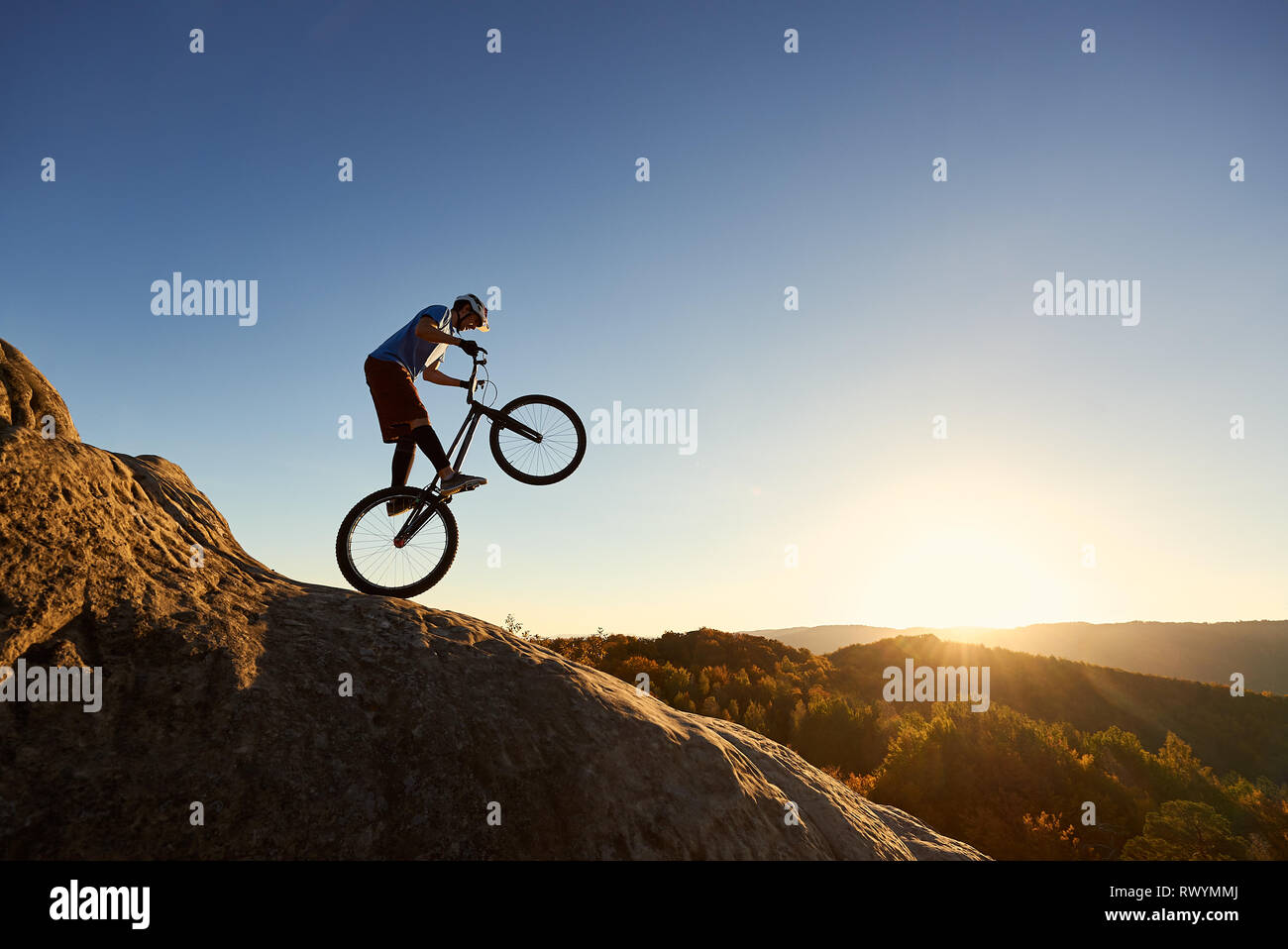 Silhouette von radprofi Reiten auf der Rückseite Rad Trial Bike. Fearless Sportler biker die akrobatischen Stunts am Rande des Big Boulder bei Sonnenuntergang. Konzept der Extreme Sport aktiven Lebensstil Stockfoto