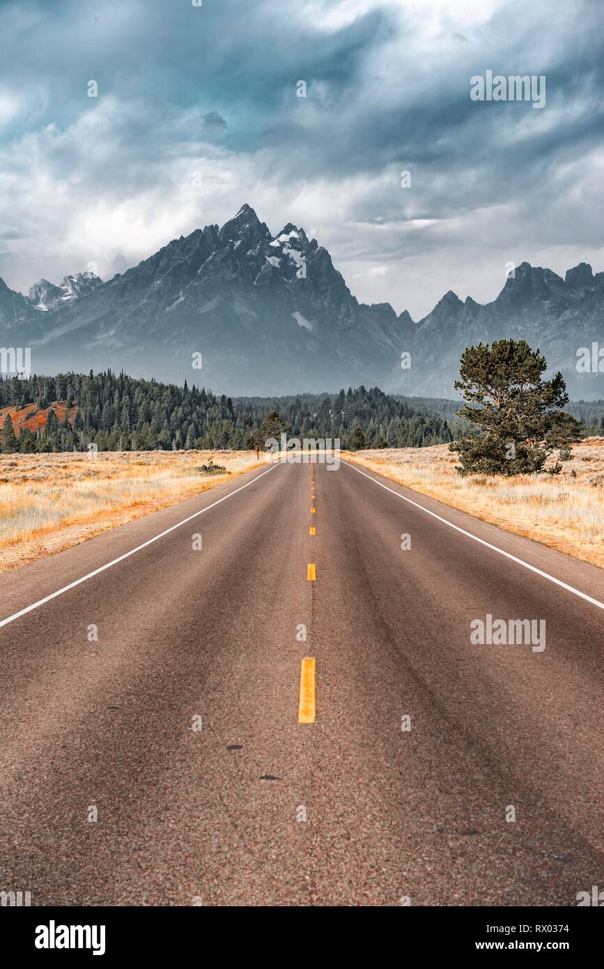 Highway vor der schroffen Berge mit bewölktem Himmel, Grand Teton Bergkette, Grand Teton National Park, Wyoming, USA Stockfoto
