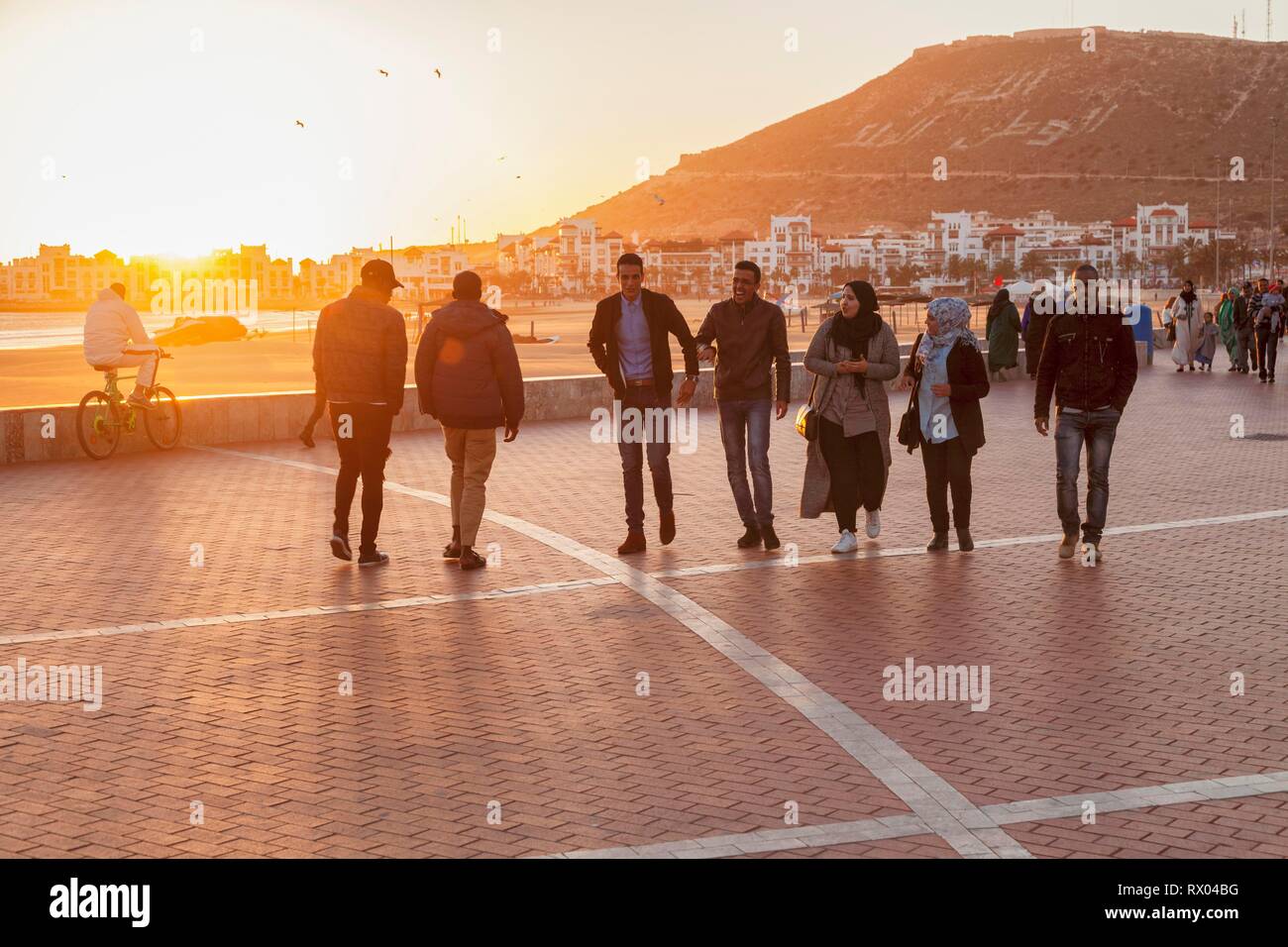 Einheimische, junge Männer und Frauen, die Promenade am Strand von Agadir bei Sonnenuntergang, Al-Magreb, Marokko Stockfoto