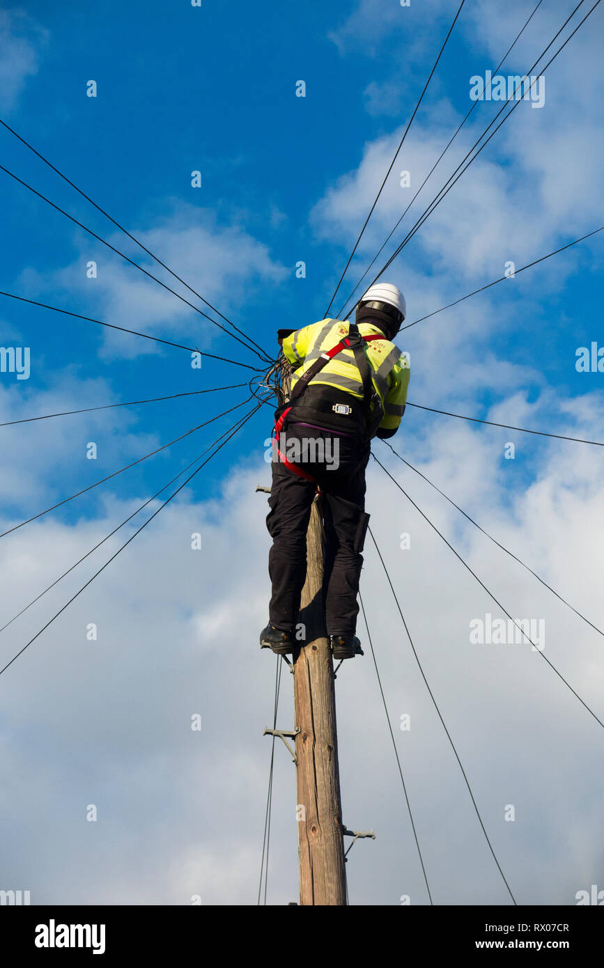 Telecom Engineer, der an inländische Telefonleitung/Breitband Internet Kupferdraht ein Telefon/Telegraphenmast in einem Londoner Straße, & blauer Himmel Stockfoto