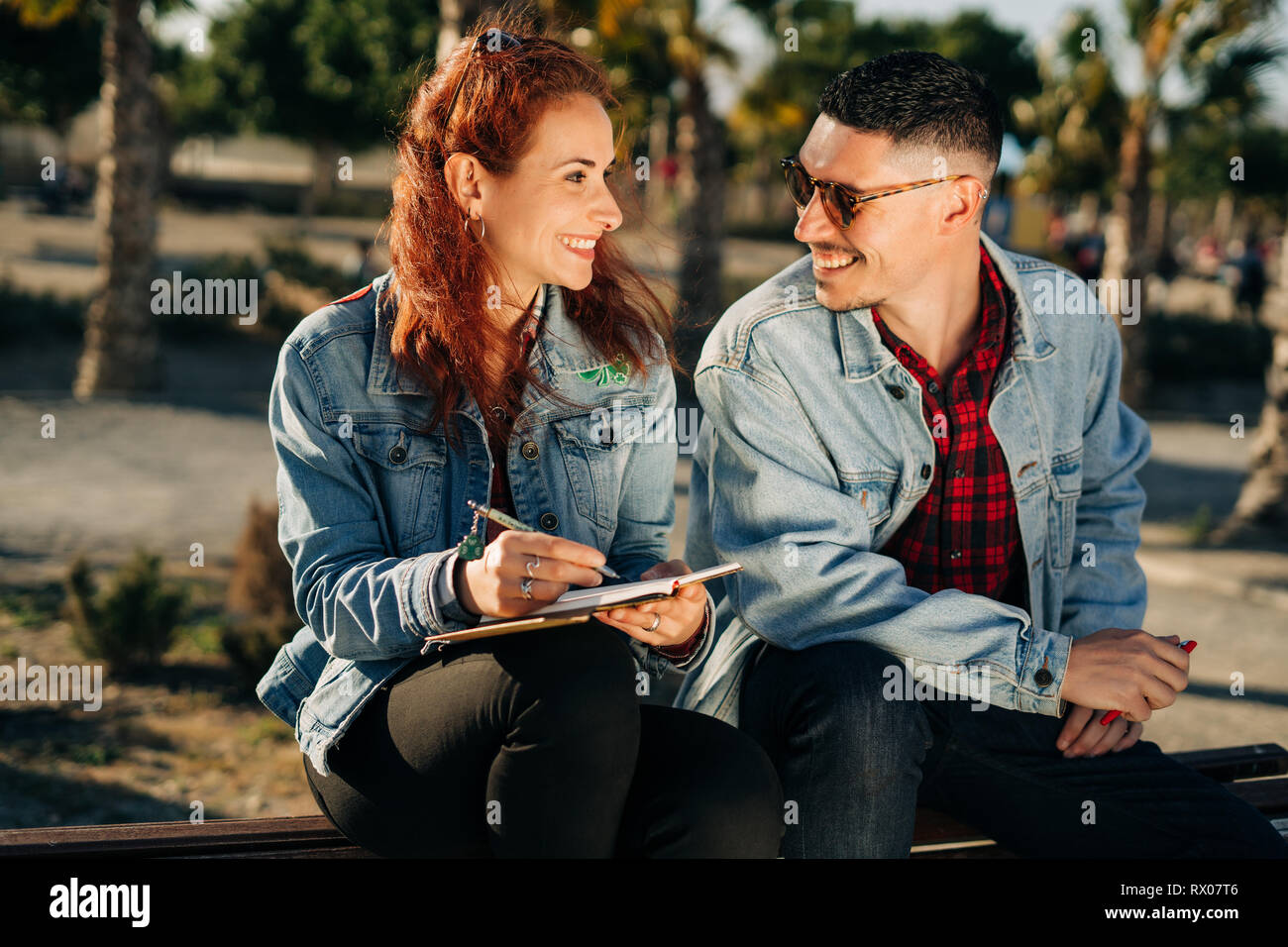 Glückliches junges Liebespaar in einem Park mit einem Buch sitzen. Stockfoto