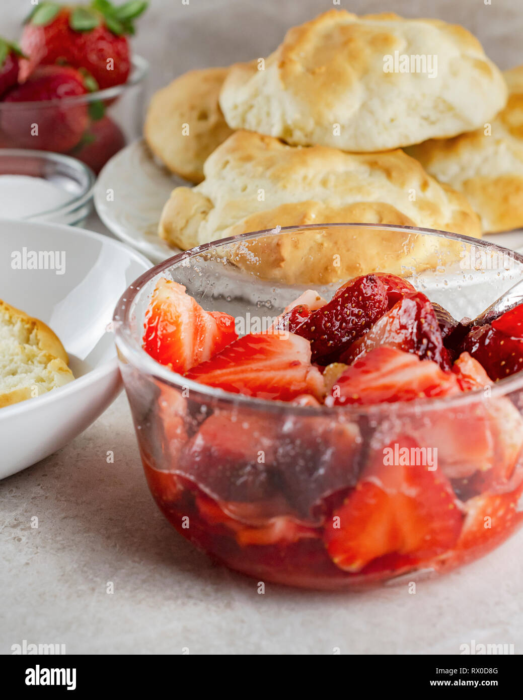 Schale in Scheiben geschnittene Erdbeeren glasiert mit Zucker. Gebäck, Zucker, und ganze Erdbeeren unscharf im Hintergrund. Stockfoto