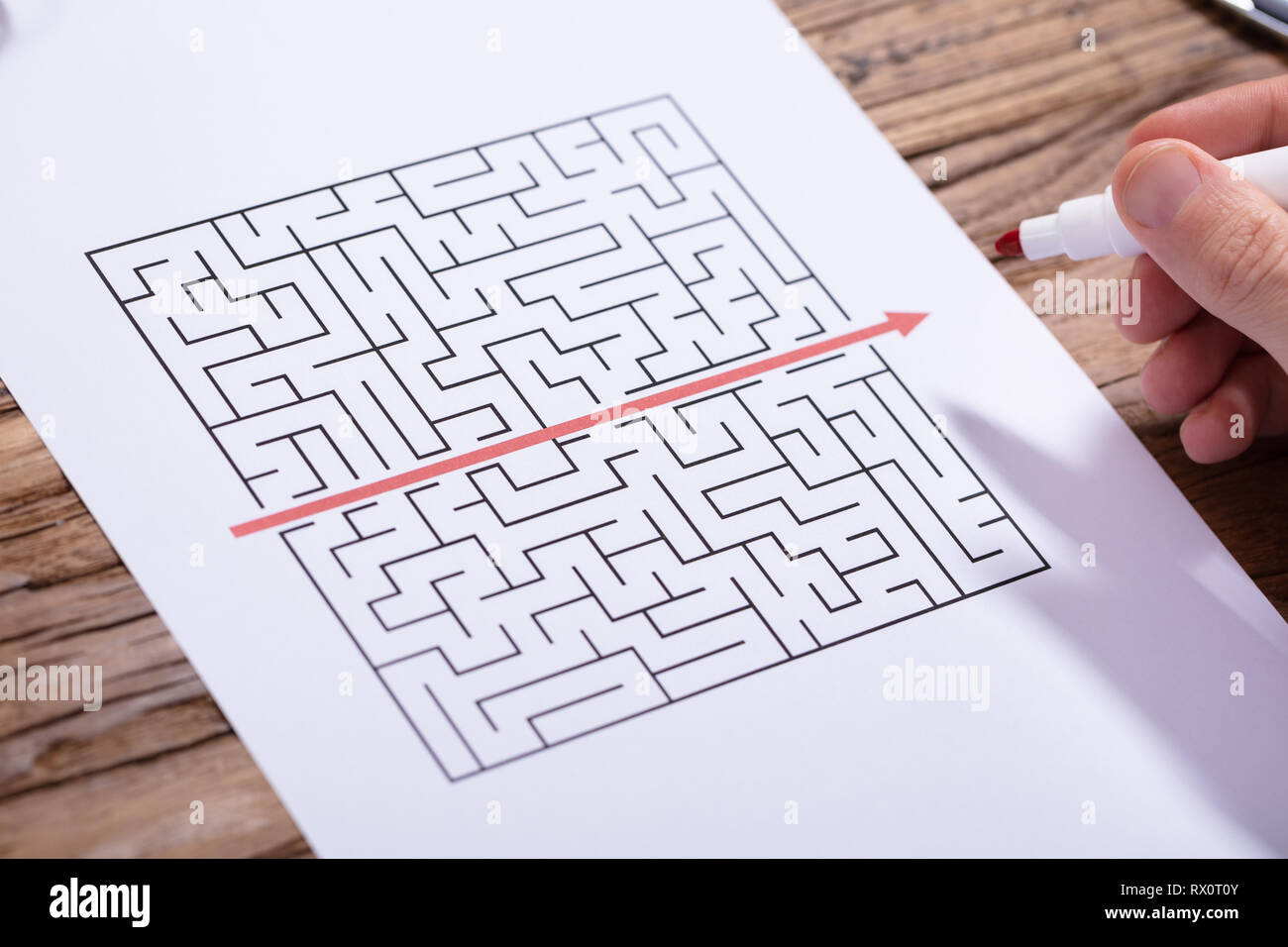 In der Nähe der Person Hand Lösung Labyrinth Puzzle mit roten Marker über Holz- Schreibtisch Stockfoto