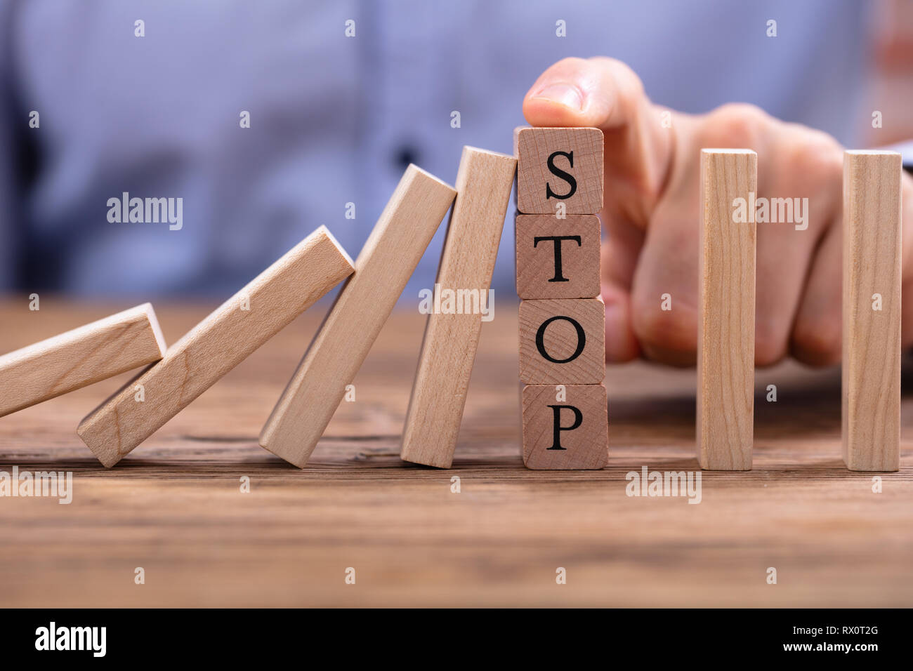 Der Geschäftsmann, der Finger über Holzblöcke mit Stop Text Anhalten fallende Dominosteine auf hölzernen Schreibtisch Stockfoto