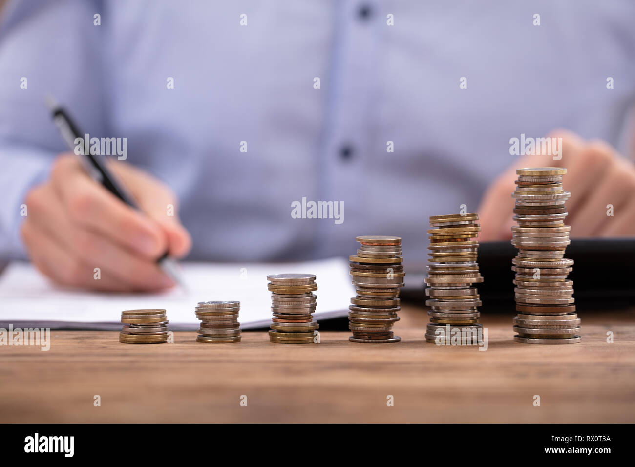 Nahaufnahme eines Geschäftsmannes Berechnung Rechnung mit Taschenrechner Vor gestapelte Münzen Stockfoto