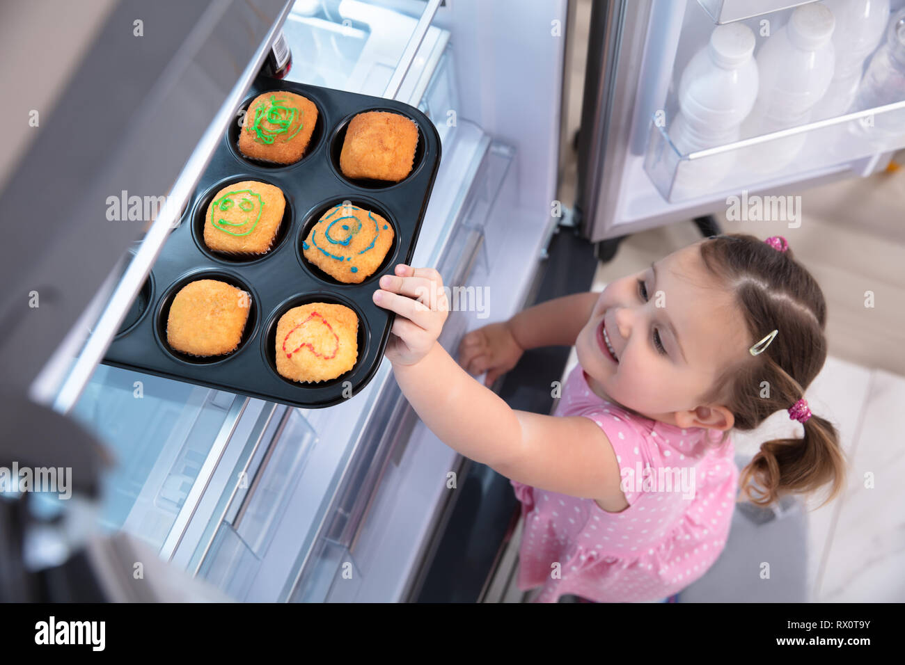 Süßes kleines Mädchen, die versuchen, zu erreichen, und kleine Kuchen aus dem Kühlschrank zu Hause abholen Stockfoto