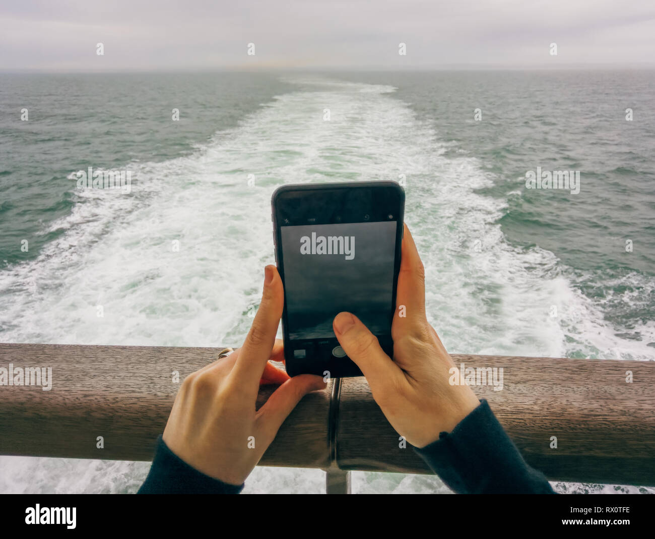 Hände halten iPhone, fotografieren Blick auf den Horizont von der Rückseite des Bootes, über dem Gefolge einer Fähre, auf See, Überquerung des Ärmelkanals, Großbritannien, Europa. Stockfoto