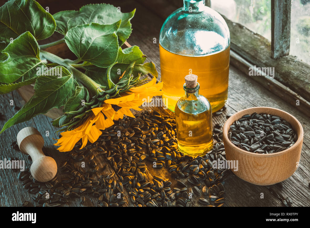 Flaschen von frischem Sonnenblumenöl, Holz- Mörtel von Samen und gelbe Sonnenblumen auf Holz- Tabelle innerhalb der retro Haus im Dorf. Stockfoto