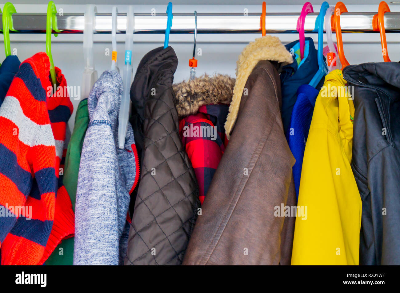 Der kleine Junge Kind größe Jacken, Mäntel und Pullover hängen in den Schrank ein Kinderparadies mit bunten Kleiderbügel. Vorbereitung für den Winter mit warme Kleidung für Kinder. Stockfoto