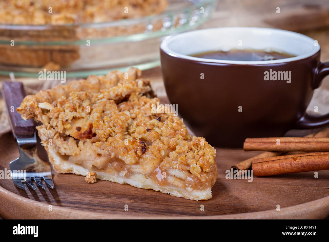 Nahaufnahme von einer Scheibe Cinnamon Apple Pie und dampfende Tasse Kaffee auf einer Holzplatte Stockfoto