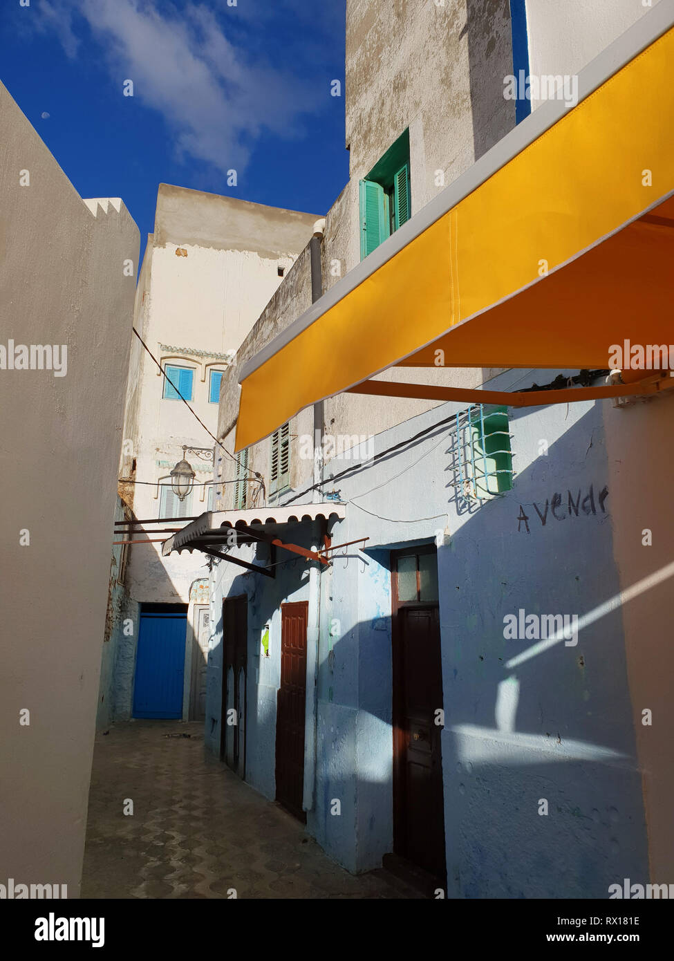 Schmale Straße mit weißen und gelben Wänden der Häuser der Medina von Asilah, blauer Himmel, Marokko. Stockfoto