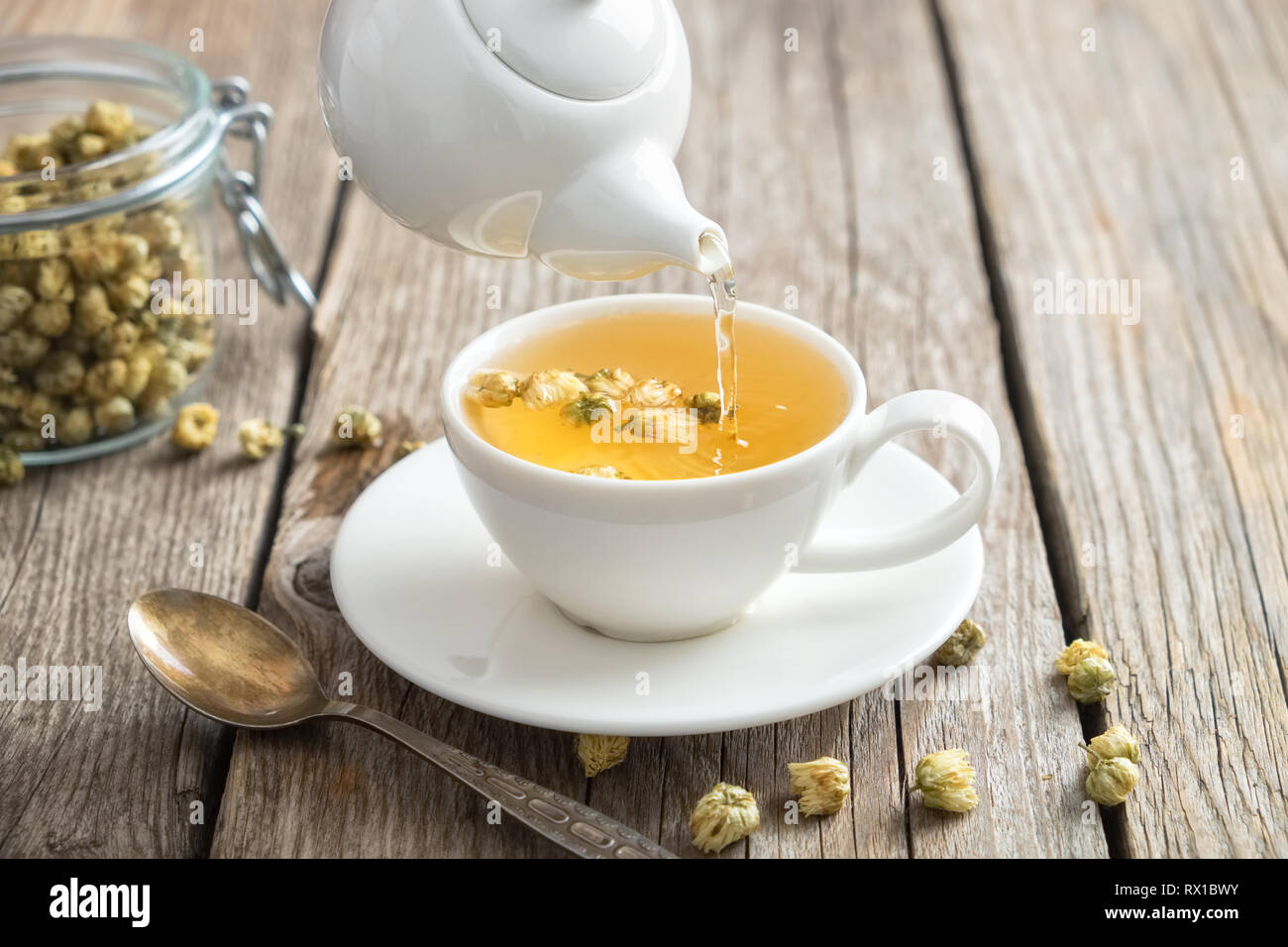 Gesunde Kamille Tee gossen in weißen Schale. Teekanne und Löffel, Glas Glas von Daisy Heilpflanzen. Stockfoto