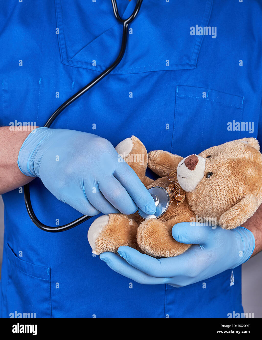 Arzt in der blauen Uniform und dem alten Latex Handschuhe mit einem braunen Teddybär, Kinderarzt behandelt ein Spielzeug Stockfoto