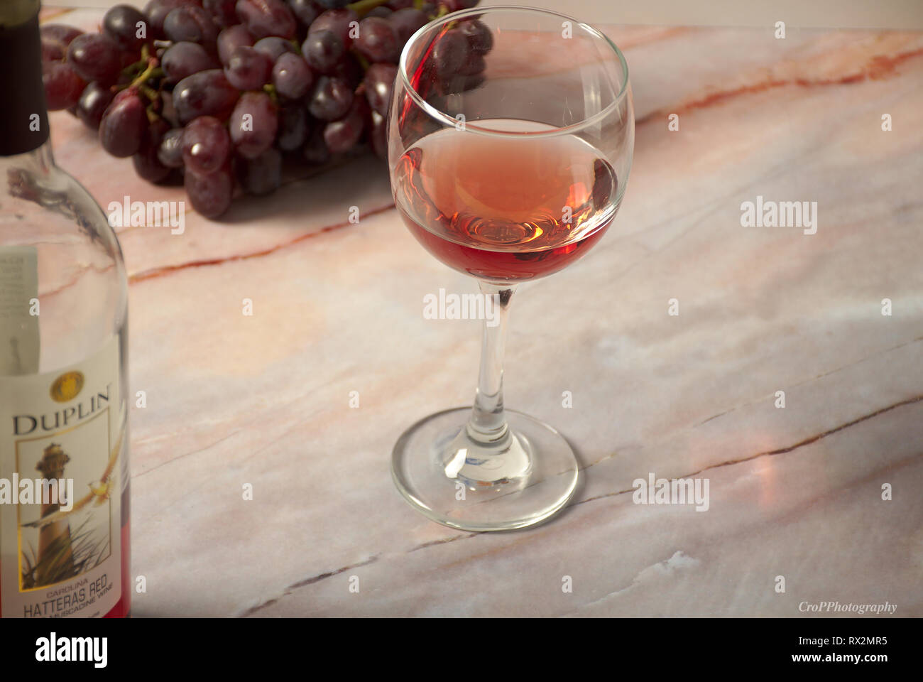 Glas Rotwein mit Flasche und Strauß roter Trauben auf Marmor tisch Stockfoto
