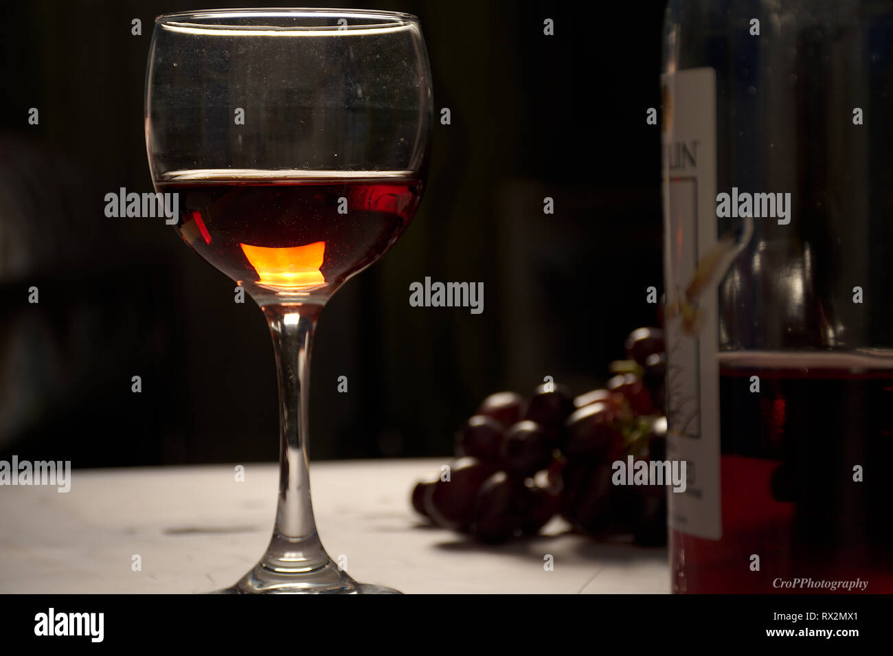 Glas Rotwein mit Flasche und roten Trauben zurück Licht Stockfoto