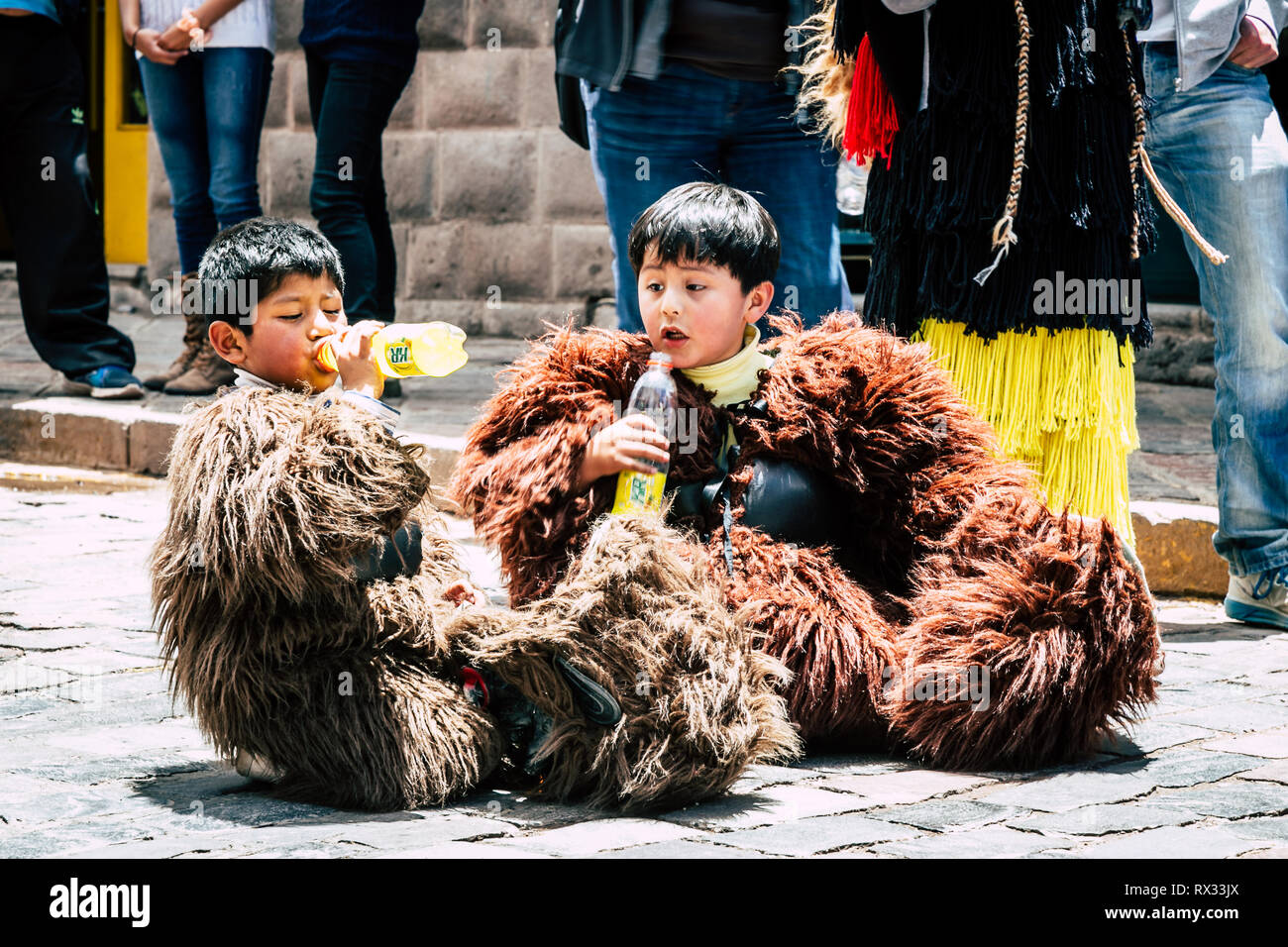 Zwei Jungs sitzen auf der Straße tragen tragen Kostüm trinken Soda an einem heißen sonnigen Tag. Ein Junge trinken während der andere schaut ihn überrascht. Stockfoto