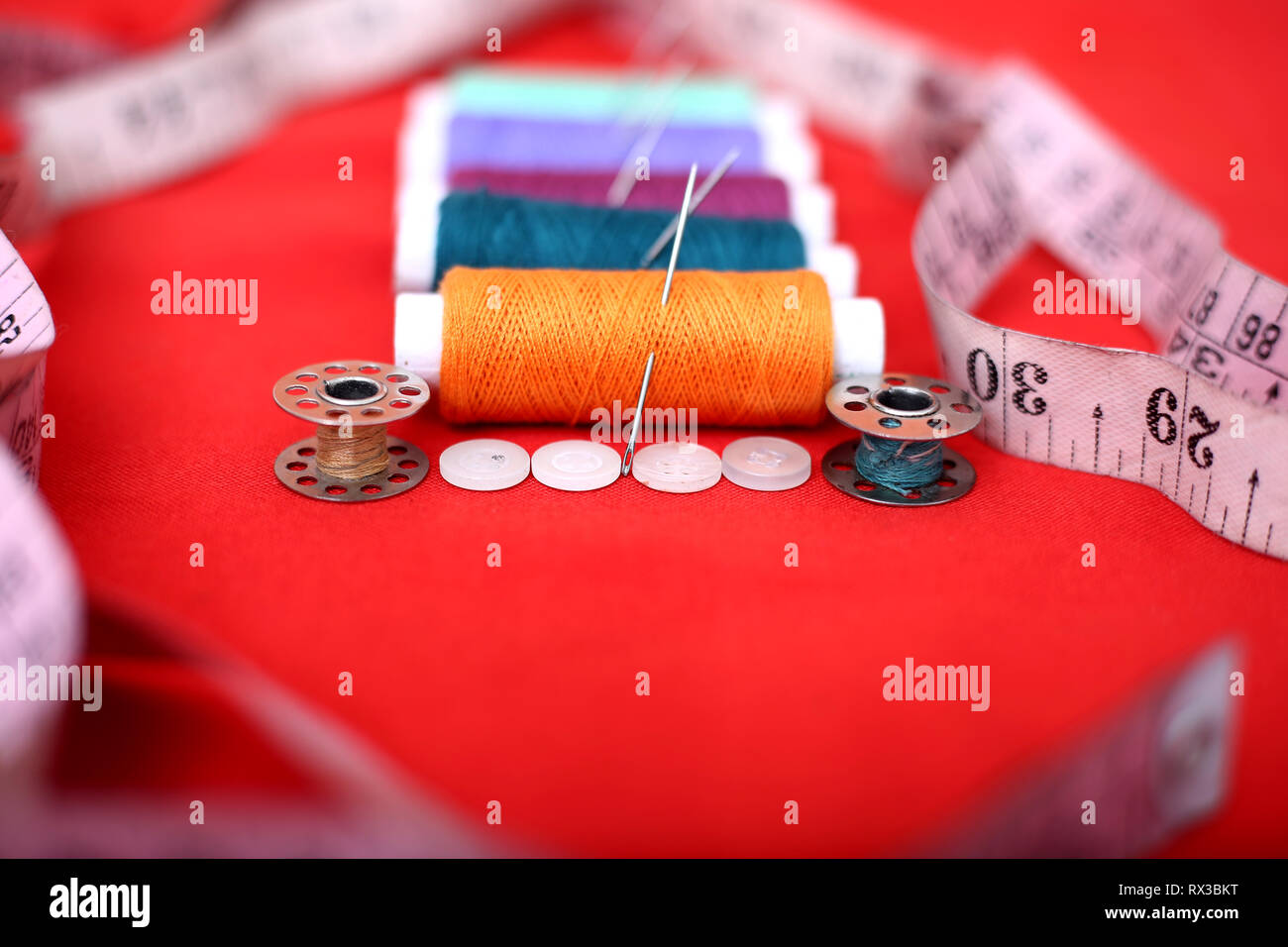 Portrait von Threads, Nadeln, Spulen, Maßband und Knopf. Auf dem roten Hintergrund. Stockfoto