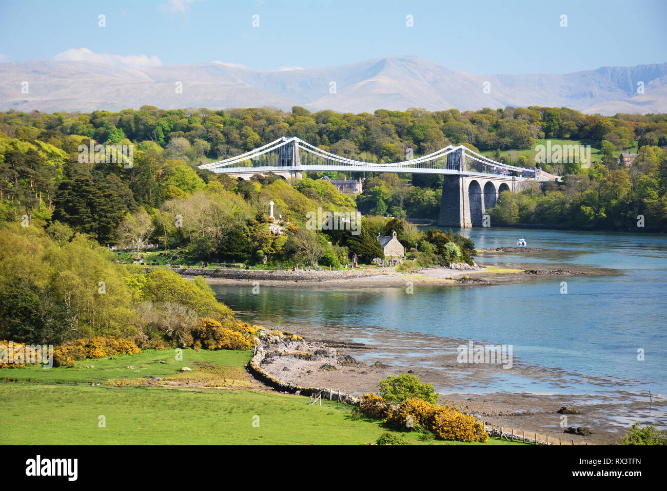 Die menai Suspension Bridge und Kirche Insel im Vordergrund bei Flut auf Anglesey im Norden von Wales. Die Berge von Snowdonia im Hintergrund. Stockfoto