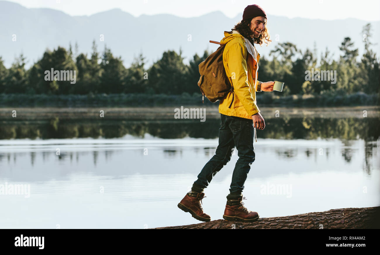 Lächelnd Mann genießen und Wandern in den Wald. Touristische gehen auf einen umgestürzten Baum am See anmelden. Stockfoto