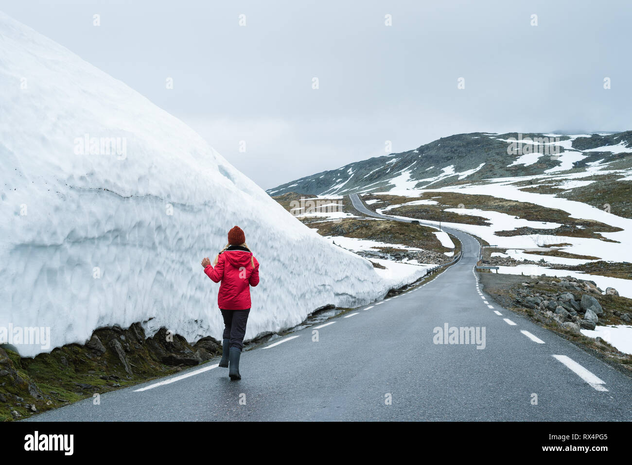 Bjorgavegen - verschneite Straße in Norwegen. Fröhliches Mädchen läuft auf einem Berg Straße in der Nähe einer Wand aus Schnee. Schwere nördlichen Landschaft Stockfoto