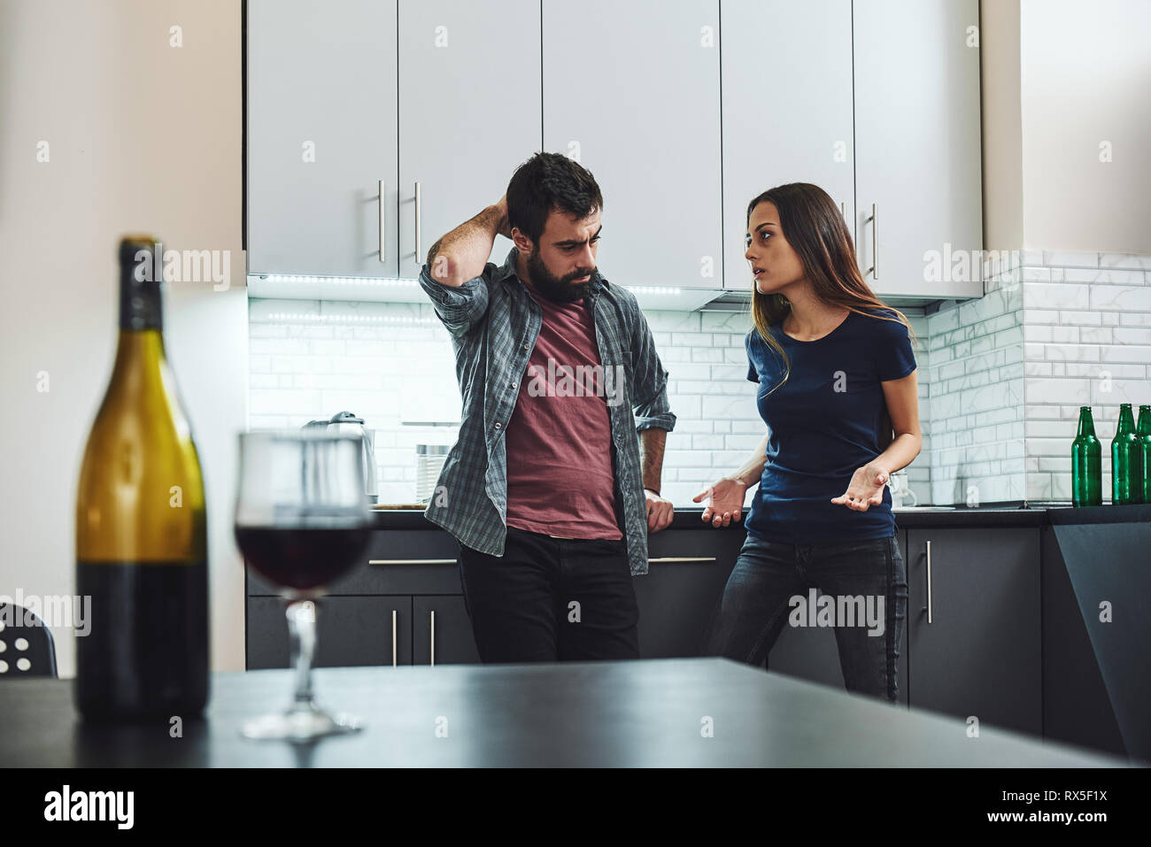 Portrait von Mann und Frau in Argument, in der Küche stehen. Eine Flasche und ein Glas Wein auf dem Tisch. Selektiver Fokus Stockfoto