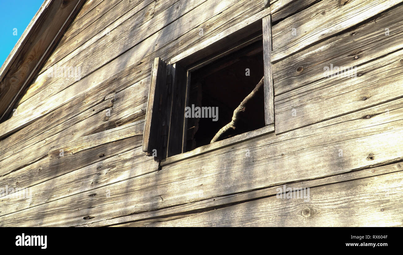 Eine Scheune mit einem Fenster. Die alten hölzernen Schuppen an der Außenseite. Blick auf die retro Bauernhaus Wand von unten nach oben. Vintage Szene mit einem beschädigten Gebäude aus Holz. Stockfoto