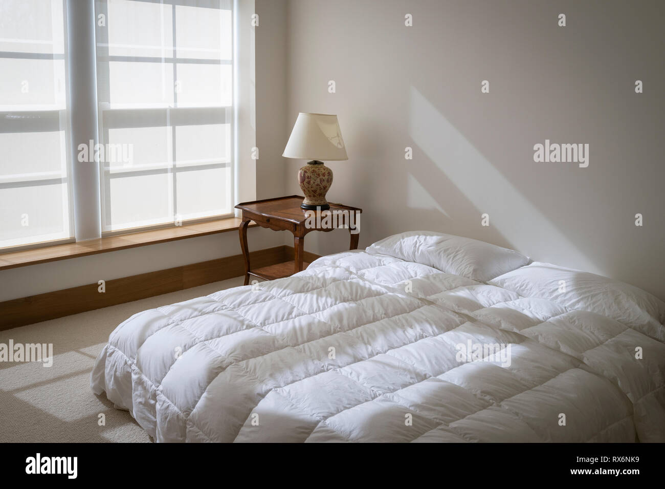 Einfache Einfache Schlafzimmer mit Sonnenlicht auf weißem Oberbett Stockfoto