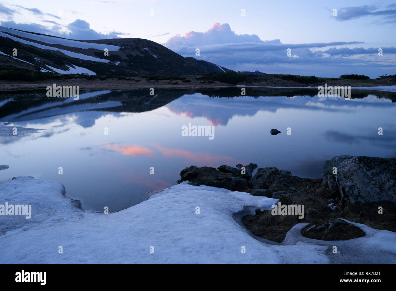 Bergsee. Dämmerung nach Sonnenuntergang. Frühling Landschaft mit dem letzten Schnee und Reflexion von Wolken im Wasser. Karpaten, Ukraine, Europa Stockfoto