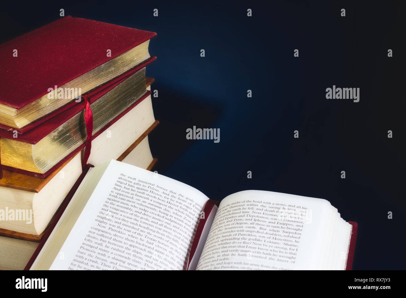 Stapel alter Bücher und ein offenes Buch gegen einen dunkelblauen Hintergrund mit Speicherplatz für eigene Text kopieren Stockfoto
